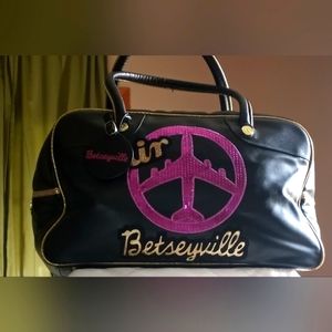 This is a Betsy Johnson synthetic leather black travel bag.